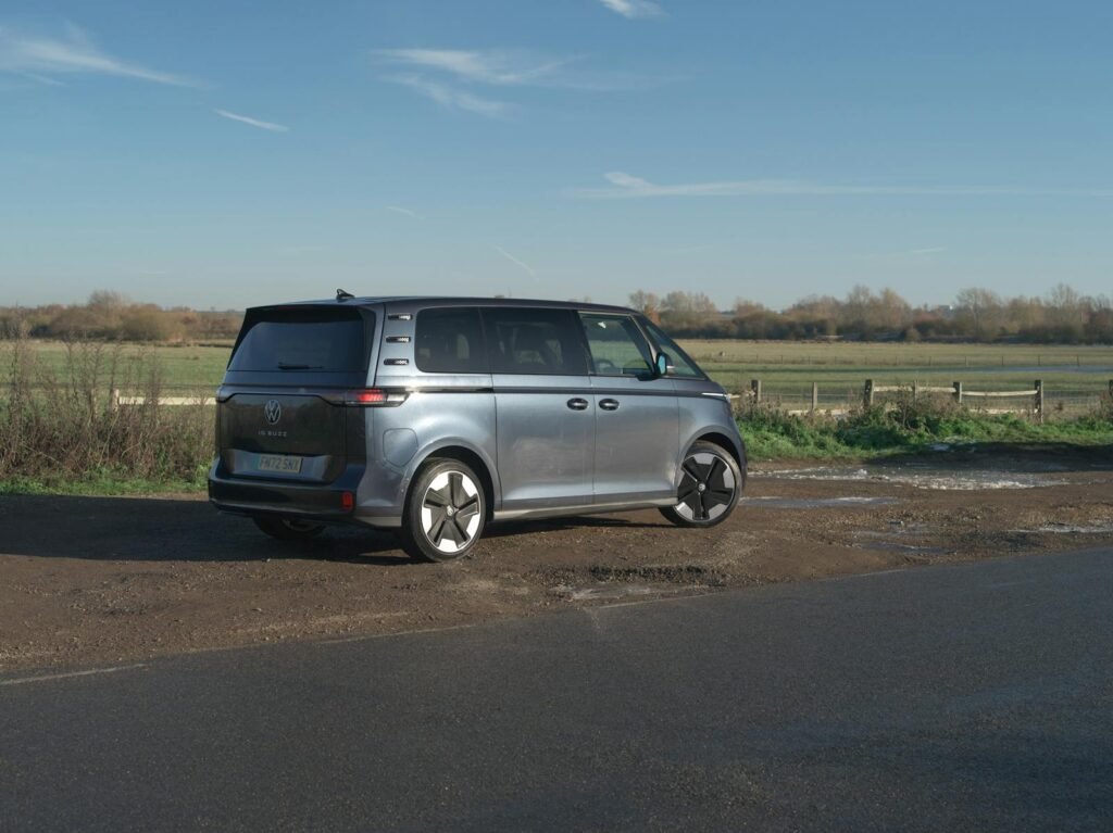 A modern Volkswagen ID.Buzz parked on a rural road with a picturesque landscape under a clear blue sky.